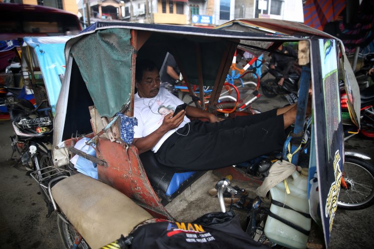 Abang becak bermain HP sambil menunggu waktu berbuka puasa di Medan