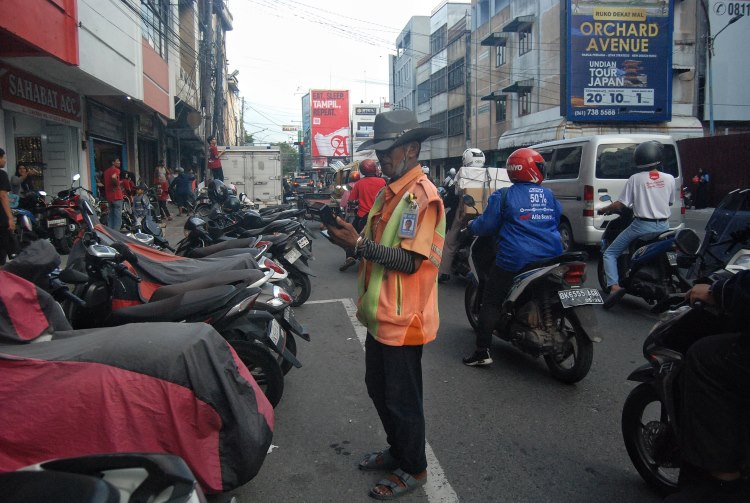 Seorang tukang parkir sedang menggunakan mesin EDC (Electronic Data Capture) sebagai alat pembayaran e-parking