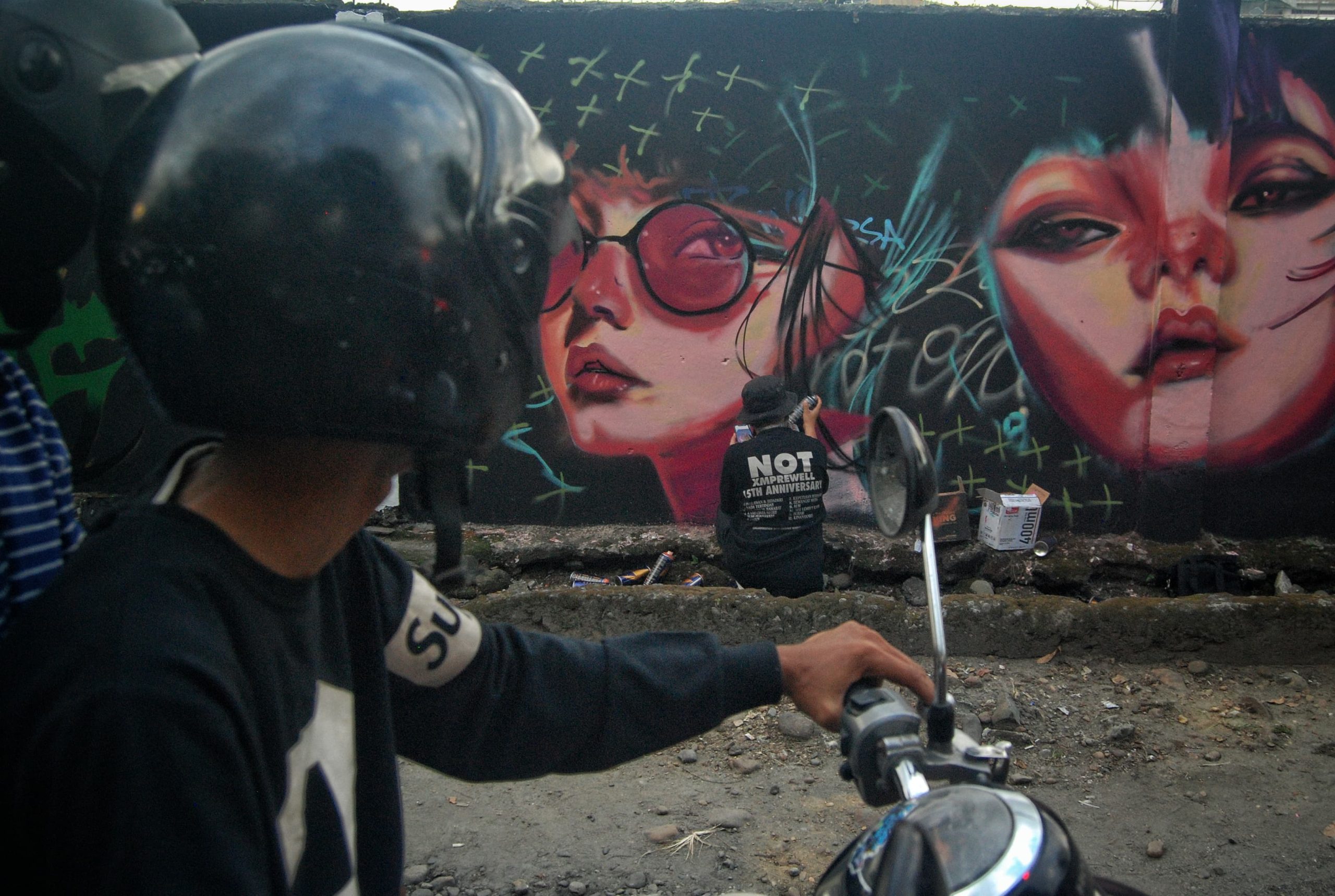 Warga melintasi seniman mural yang melukis di sepanjang Jalan Adam Malik, Medan, Sumatera Utara